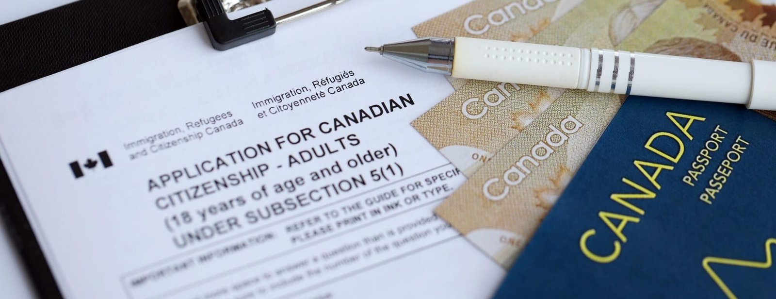 Application for Canadian citizenship for adults on table with pen, passport and dollar bills