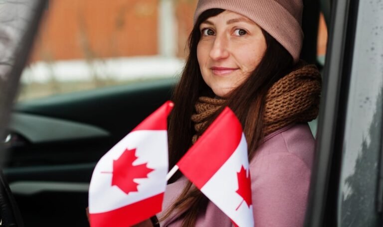 Young woman with Canada flag siting on car.