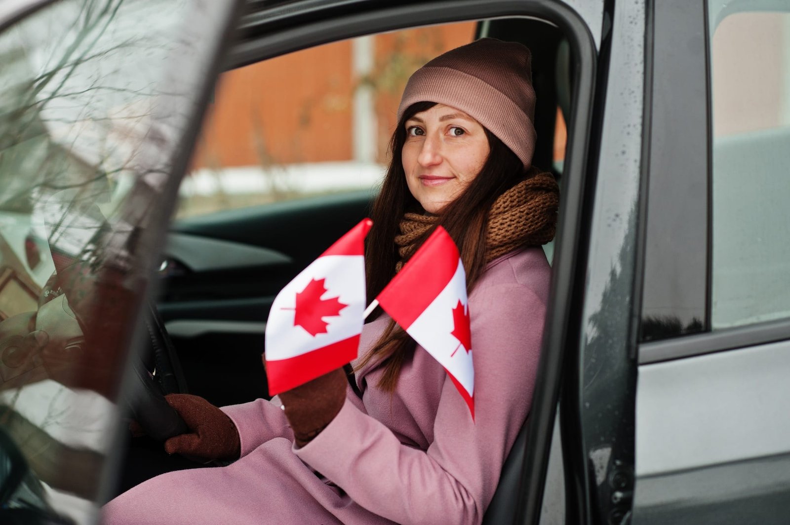 Young woman with Canada flag siting on car.