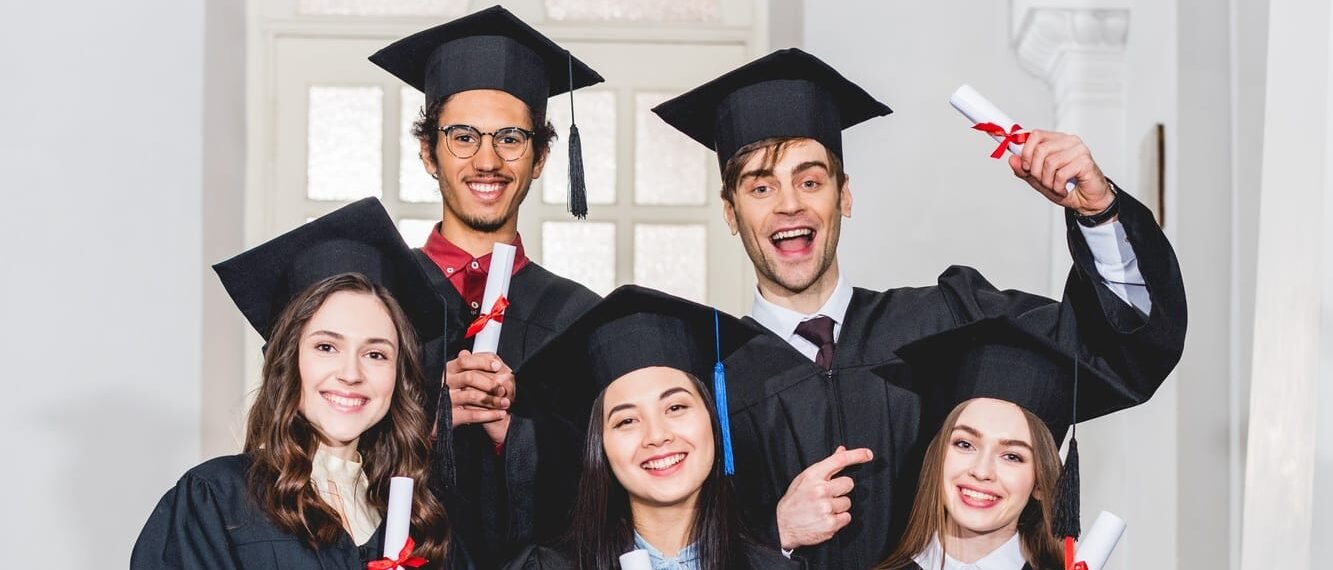 cheerful group of students in graduation gowns holding diplomas