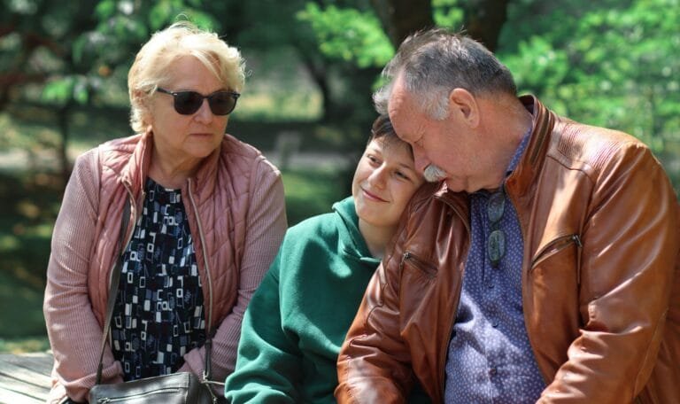 Grandmother with grandfather and grandson sit on a bench in the park.