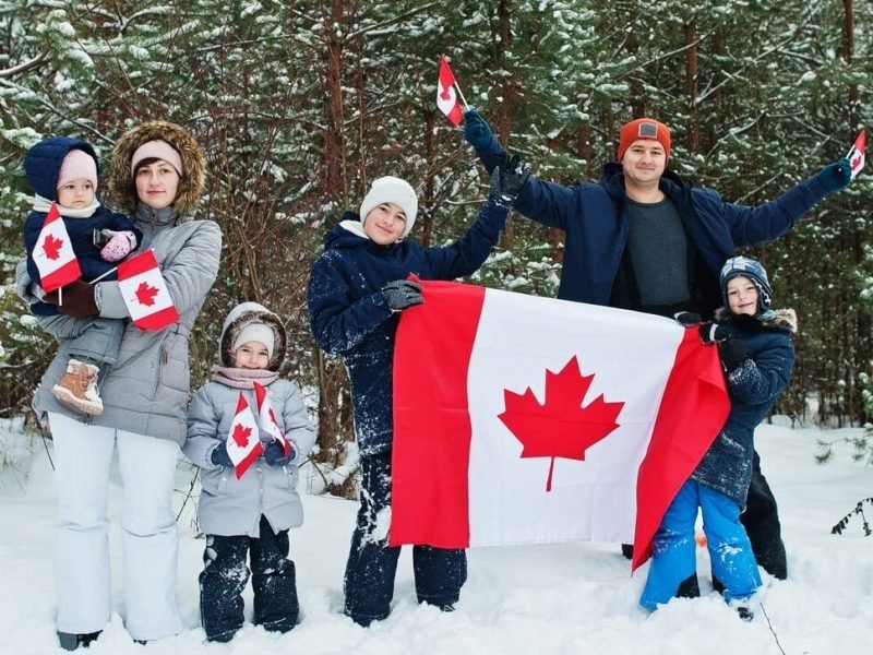 Family holding flag of Canada on winter landscape.