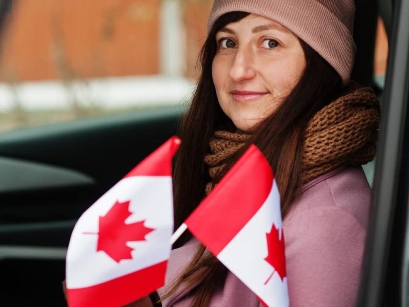 Young woman with Canada flag siting on car.